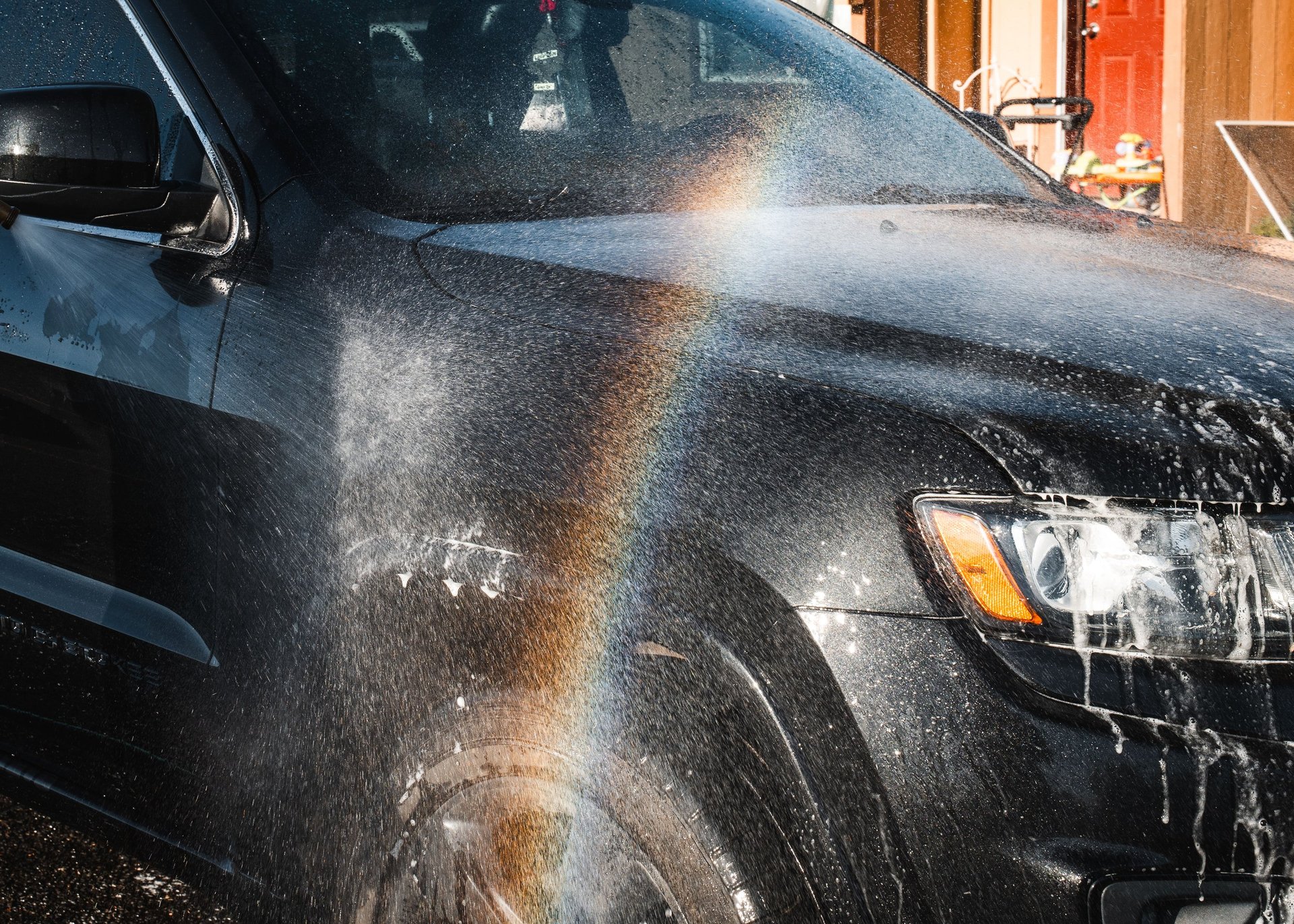 Black truck being washed with water spray and soap suds covering the hood and windshield